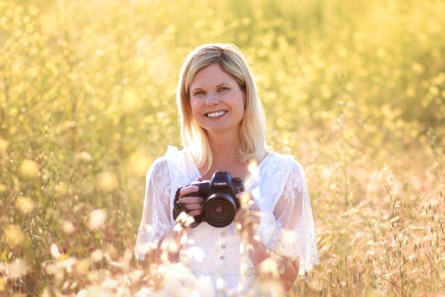 Photographer holding camera sitting in field