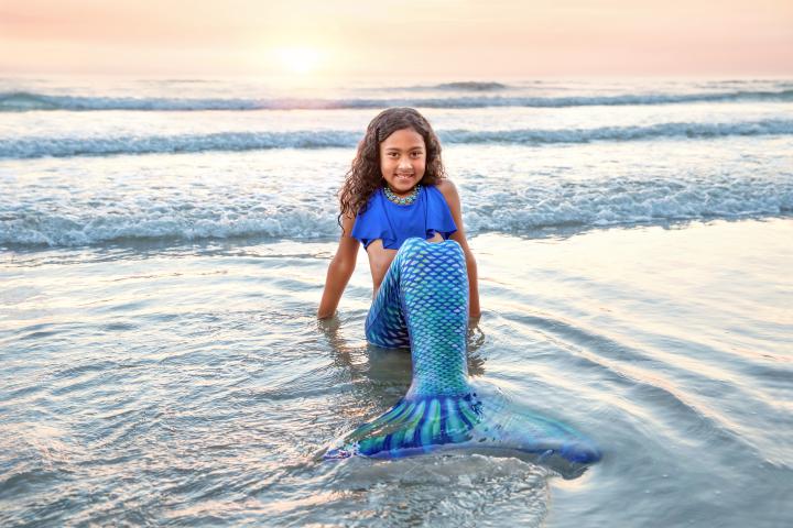 Little girl dressed as a mermaid sitting in the waves